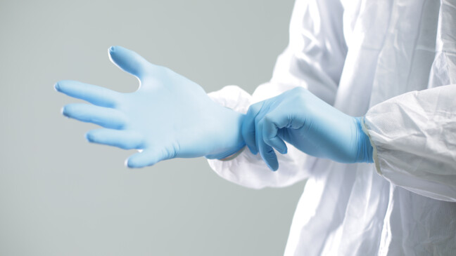 Doctor,In,A,Protective,Suit,Puts,On,Blue,Rubber,Gloves